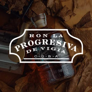 Produktfoto einer Rum-Flasche ‚Ron La Progresiva de Vigía Cuba‘, liegend auf einer Oberfläche aus Eis und Holzstücken, aufgenommen mit warmem Licht zur Hervorhebung der Glasstruktur.